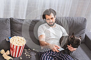 irritated loner watching tv with with bulldog on sofa in living