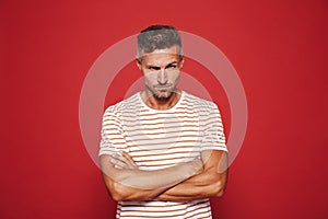 Irritated man 30s in striped t-shirt standing with arms crossed