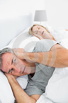 Irritated man blocking his ears from noise of wife snoring