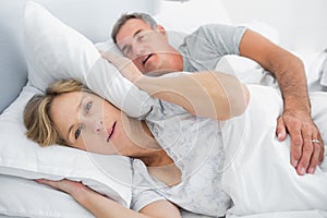 Irritated wife blocking her ears from noise of husband snoring