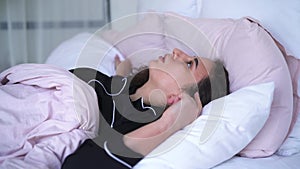 Irritated woman closing ears with pillow. Portrait of young annoyed caucasian girl trying to sleep despite of noise