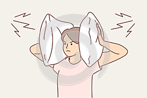 Irritated woman covers ears with pillow so as not to hear noise from neighbors who are having party