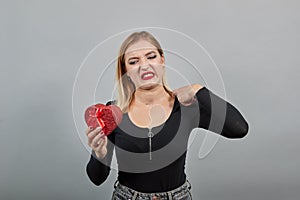 Irritated woman holds a gift in her hand red heart, a bad mood