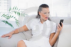 Irritated woman in white dress looking at her smartphone