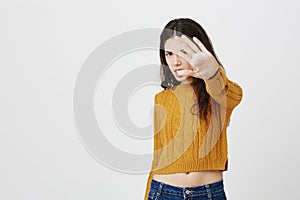 Irritated young european celebrity covering face with stretched hand, expressing disgust and dislike while standing over