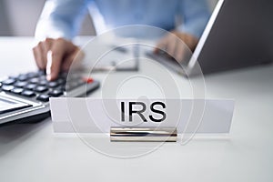 IRS Nameplate In Front Of Accountant Calculating Tax