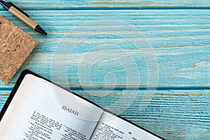 Isaiah open Holy Bible Book on a rustic wooden background with a notebook and pen