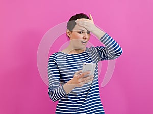 isappointed-faced girl looks at her cell phone as she stands in front of a pink background