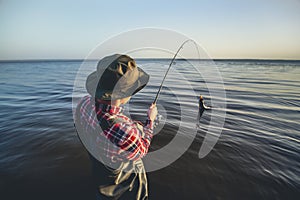 Isherman with a fishing rod in his hand and a fish caught stands in the water