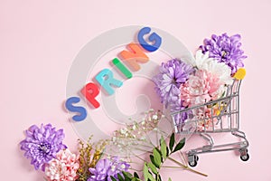Ishopping troley, nscription spring in flowers on a pink background top view spring mood concept