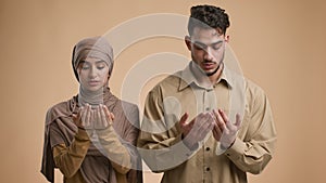 Islamic Couple Praying Holding Hands In Prayer Gesture, Beige Background
