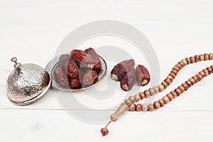 Islamic festival of Ramadan concept. with a delicious tropical dates on a silver plate and shiny rosary on a white wooden table ba