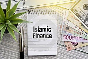 ISLAMIC FINANCE text with notepad, keyboard, decorative vase, fountain pen, and banknotes currency on wooden background