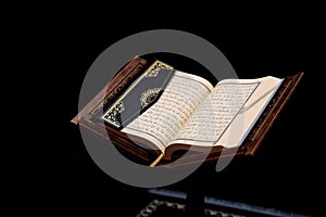 Islamic Holy Book Quran on wood carving rahle with rosary beads and prayer rug on black background. Kuran the holy book of Muslims