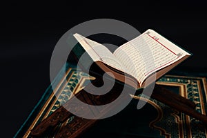 Islamic Holy Book Quran on wood carving rahle with rosary beads and prayer rug on black background. Kuran the holy book of Muslims