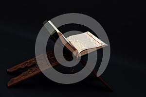 Islamic Holy Book Quran on wood carving rahle with rosary beads and prayer rug on black background. Kuran the holy book of Muslims photo