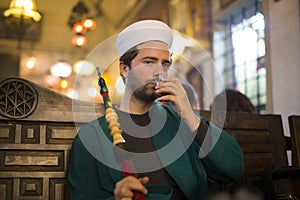 islamic man with traditional dress smoking shisha, drinking tea