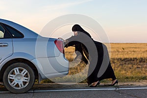 An Islamic woman is pushing a car along the road. Woman driver - car breakdown