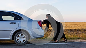 An Islamic woman is pushing a car along the road. Woman driver car breakdown