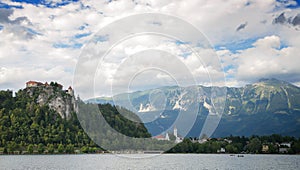 The island of Bled, Bled castle on cliff, Julian Alps and Church of the Assumption, the front ground is stone and sea water, Bled