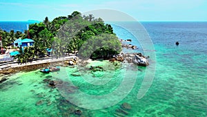 An island with clear sky above in and crystal clear sea water swashing over the beach