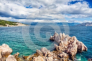 Island cliffs and waves in the ocean, seen from coastline. Calm water, clear sky and waves on a sunny summer day