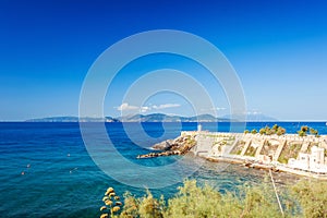 Island of Elba on horizon visible against lighthouse and Piazza Bovio in Piombino, Tuscany