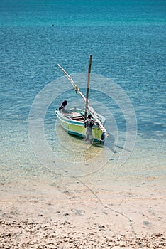 A fisherman at a small fishing boat moored in the shallow water at the beach.