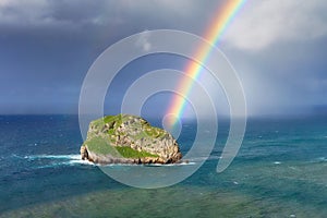 Island named Aketxe in Bermeo with stormy clouds and a rainbow