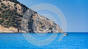 An island with trees in the Mediterranean Sea and a boat on the blue sea