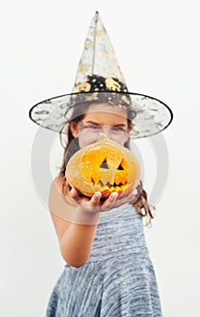 Isnt my pumpkin just bootiful. Shot of a little girl wearing a witch hat while holding a jack o lantern against a white