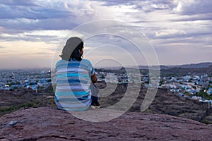 isolate girl watching city landscape at mountain top with dramatic sky at dusk