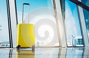 Isolate traveler tourist yellow suitcase at floor airport on background large window sun flare, bright luggage waiting in departur