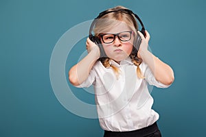 Pretty, cute little girl in white shirt, glasses, black trousers and headphones