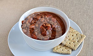 Isolated bowl of chili soup with whole wheat saltine crackers.