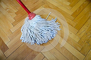 Isolated cleaning mop with red wooden stick on wooden home floor,parquet,  cleaning and disinfection of surfaces , close up
