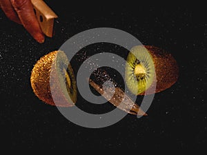 Isolated closeup shot a knife slicing kiwi fruit mid-air in front of a black background