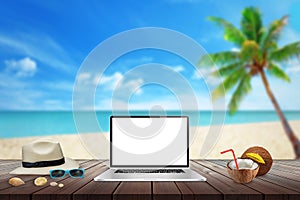 Isolated display of laptop on wooden table for mockup. Beach, sea, palm and blue sky in background.