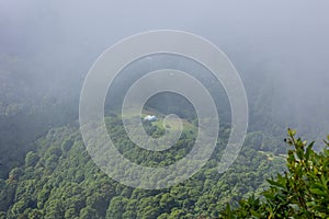 An isolated farm house surrounded by mist on a ridge in the forest