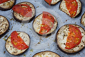 Isolated filled frame close up shot of baked sliced aubergine eggplant with thin tomato slices on top, sprinkled with dry green
