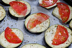 Isolated filled frame close up shot of uncooked raw sliced aubergine eggplant with thin tomato slices on top sprinkled with dry