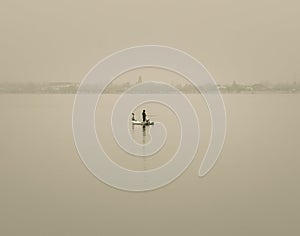 Isolated fisherman standing in a boat in the middle of the lake with a rod in in his hand. Man fishing