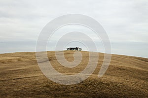 Isolated idyllic peaceful farm house building on top of a grass meadow field hill on cloudy day in South Iceland Europe