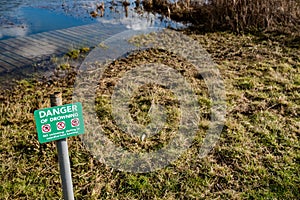 Isolated image of a Danger Sign seen positioned near a deep, open river and adjacent quick sands.