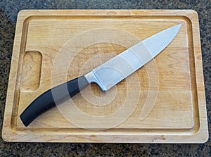 Isolated large chefâ€™s knife on a large wooden cutting board with a granite kitchen counter