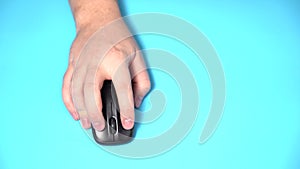 Isolated on a Light Blue Background. Male Hand Holds Wireless Computer Mouse on the Table. Click and Move