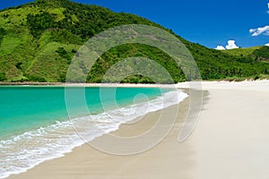 Isolated lonesome lagoon with turquoise sea, white surf in shallow water, white soft sand and lush green hill