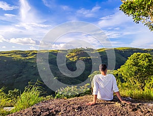 isolated man sitting at mountain top with bright blue sky at morning from flat angle