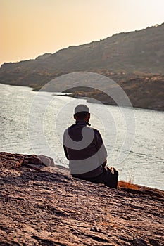 isolated man sitting at mountain top with lake view backbit shot from flat angle