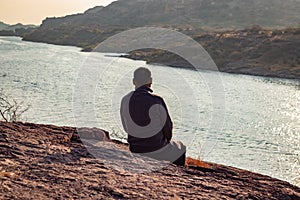 isolated man sitting at mountain top with lake view backbit shot from flat angle